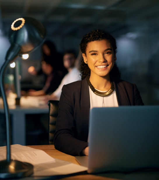 Female worker smiling to the camera with a book and a laptop in a library setting