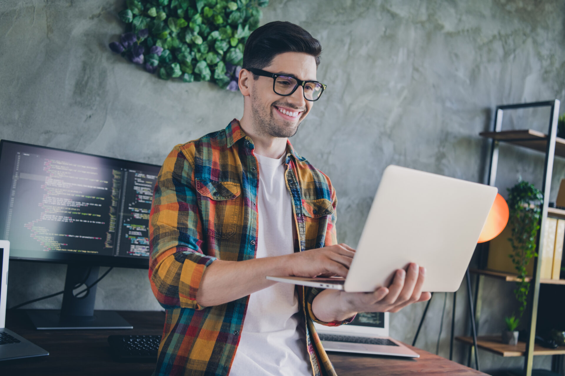 Male data analyst smiling and reviewing code lines in a laptop screen while working at a modern office