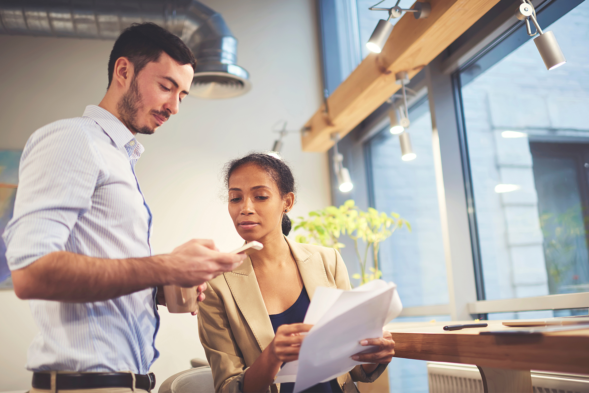 A man and woman stand together in front of a desk, engaged in conversation or collaboration