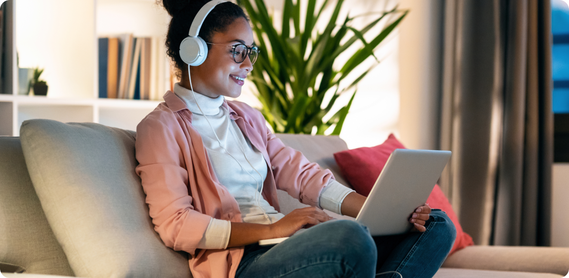 A woman with headphones sits on a couch, focused on her laptop, enjoying her navigation experience while checking her finances