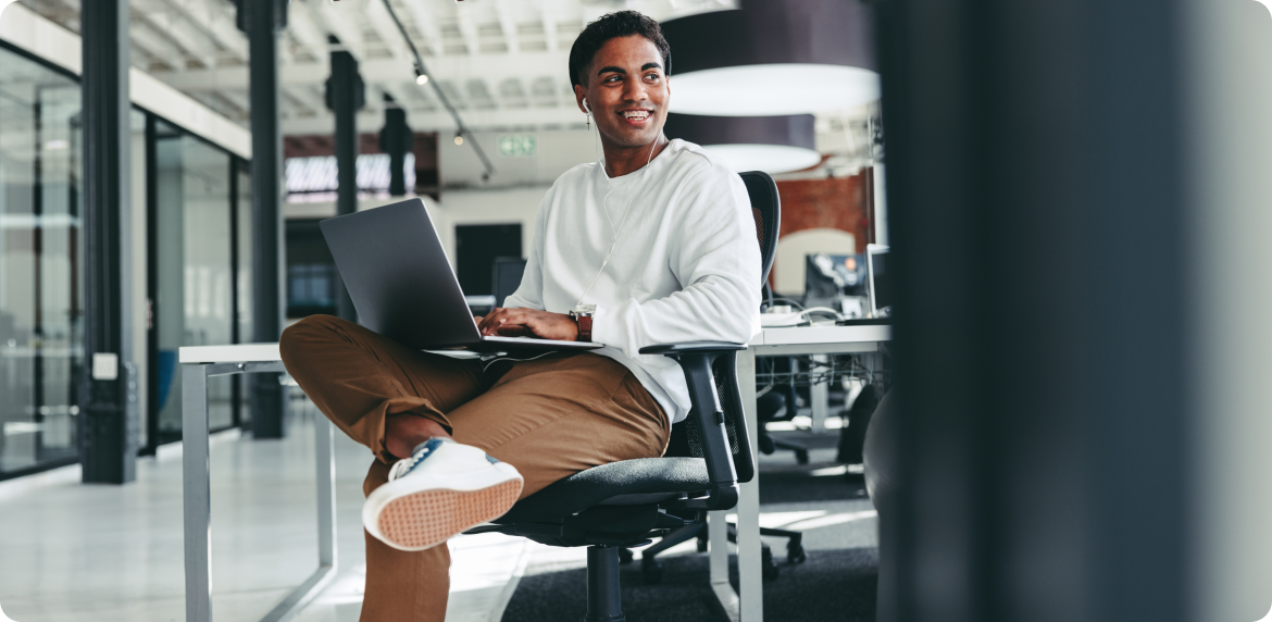 A sales professional seated on a chair, focused on his laptop, engaged in work