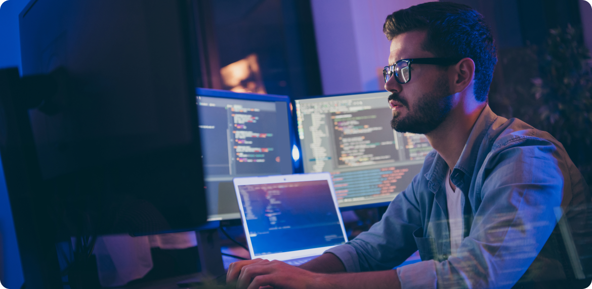 A real estate professional wearing glasses focused on work with two computer monitors in front of him