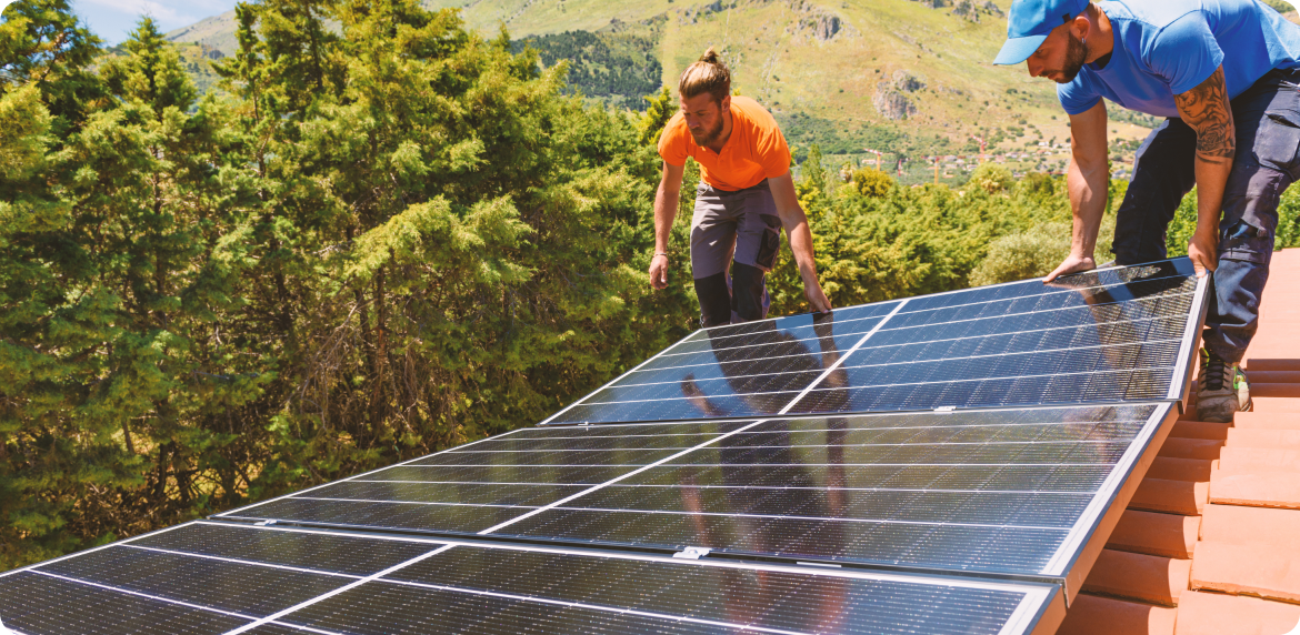 Two male engineers installing a solar panel in a rooft while wearing security gear in daylight.