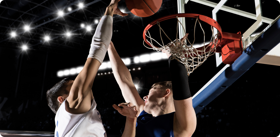 Two male basketball players shooting a basket and competing in a tournament game.