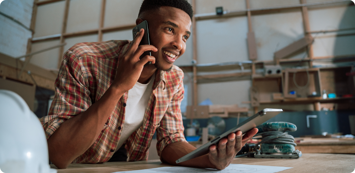 Male warehouse manager talking through the phone and reviewing business data in a tablet.