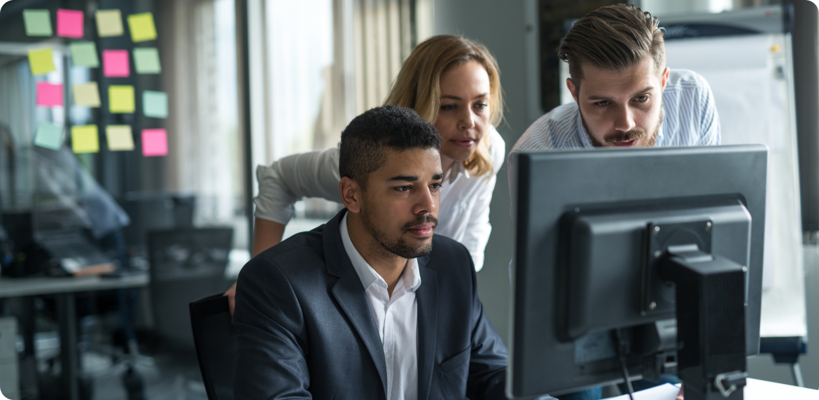 Three coworkers, two male and one female staring at a computer screen in an office setting