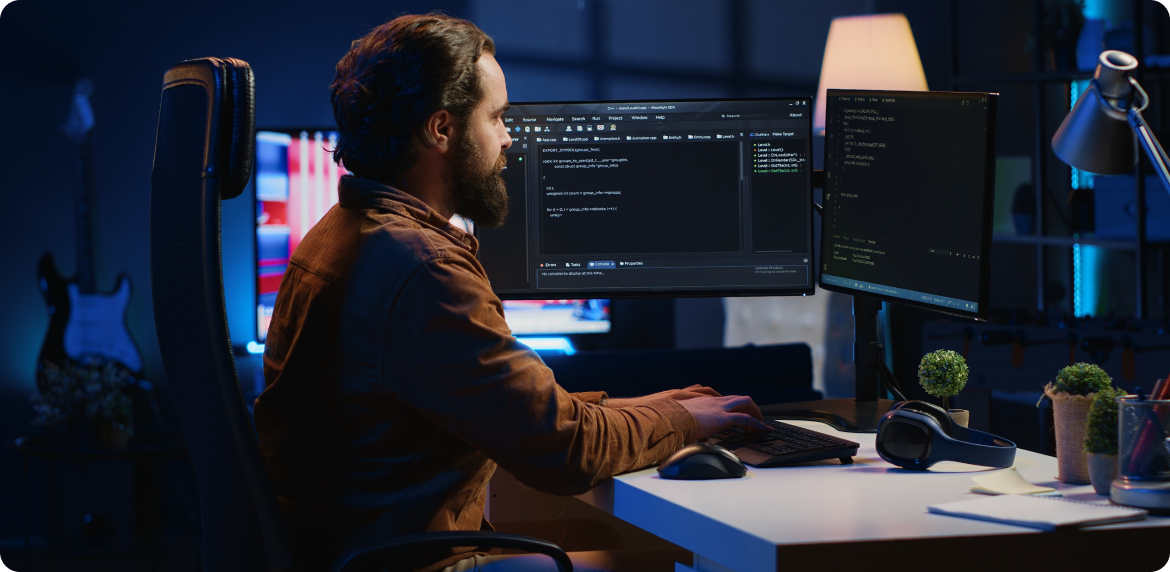 Male software developer reviewing code in a dual screen monitor at an office setting.