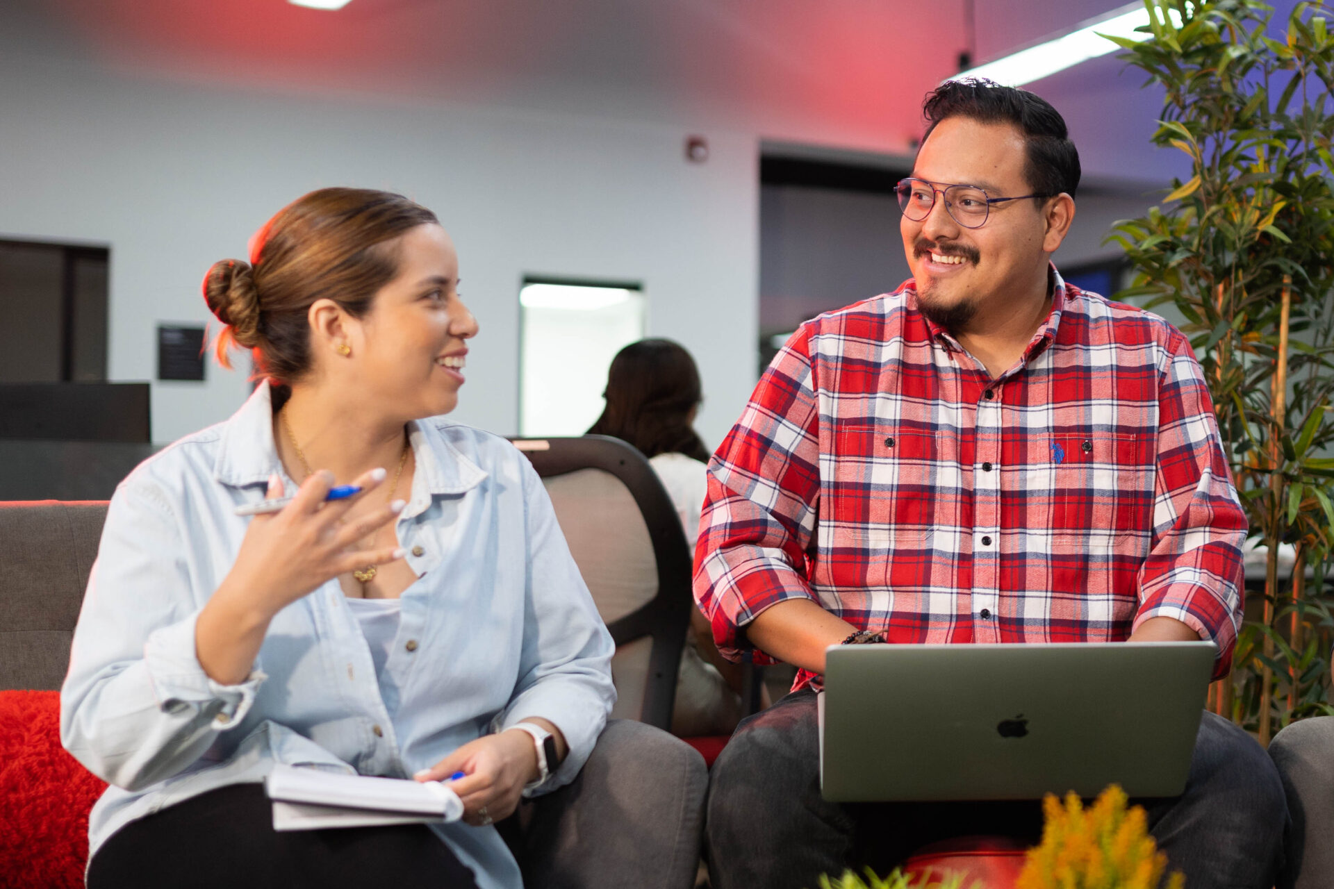 Two Applaudo employees sitting on a couch, each focused on their laptops, engaged in a collaborative work session.