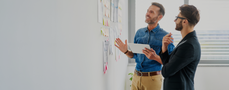 Two men discussing ideas while standing in front of a whiteboard filled with notes and diagrams.