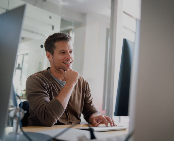 A man smiles warmly while seated at a desk, exuding a sense of contentment and professionalism.