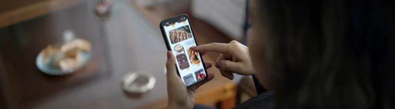 A woman orders food using her smartphone while sitting at a table.